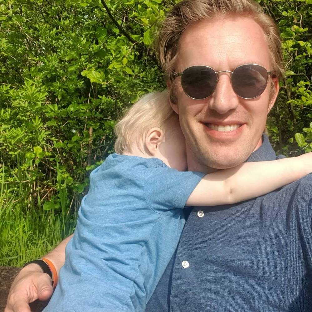Guido smiling in sunglasses while a toddler hugs him tightly around the neck.