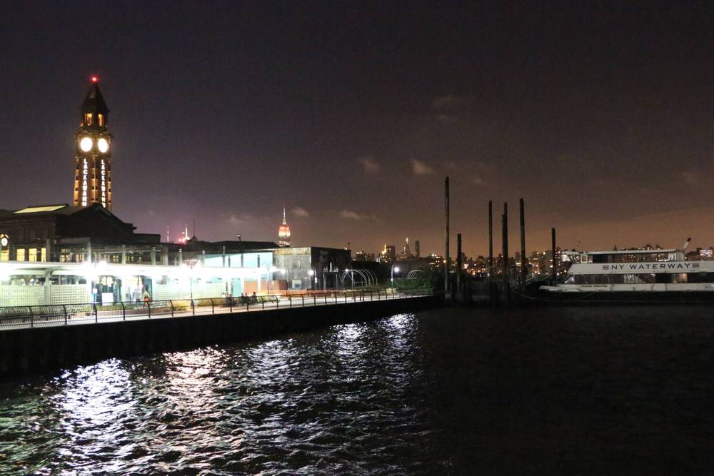 A lit pier clock tower and ferry terminal stand along the water's edge at night.