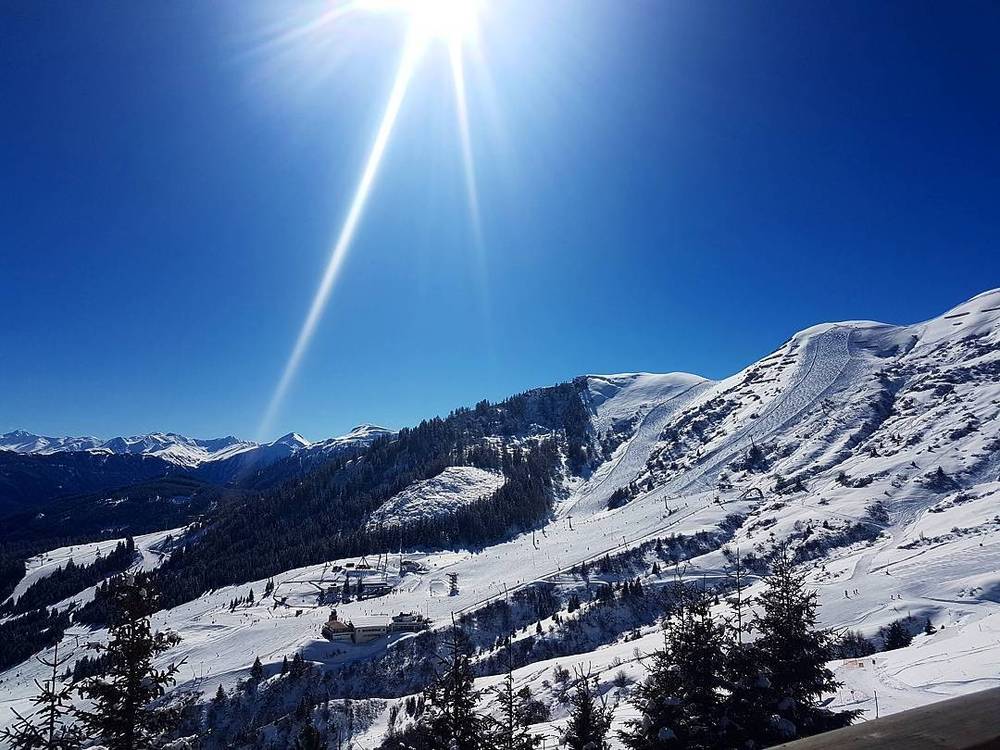 A sunlit panorama of snow-covered alpine peaks and a ski resort below.
