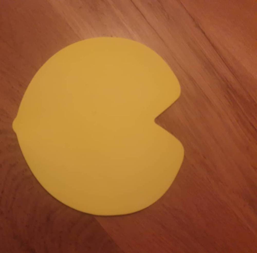 A yellow, Pac-Man-shaped piece of fabric or foam lying on a wooden floor.