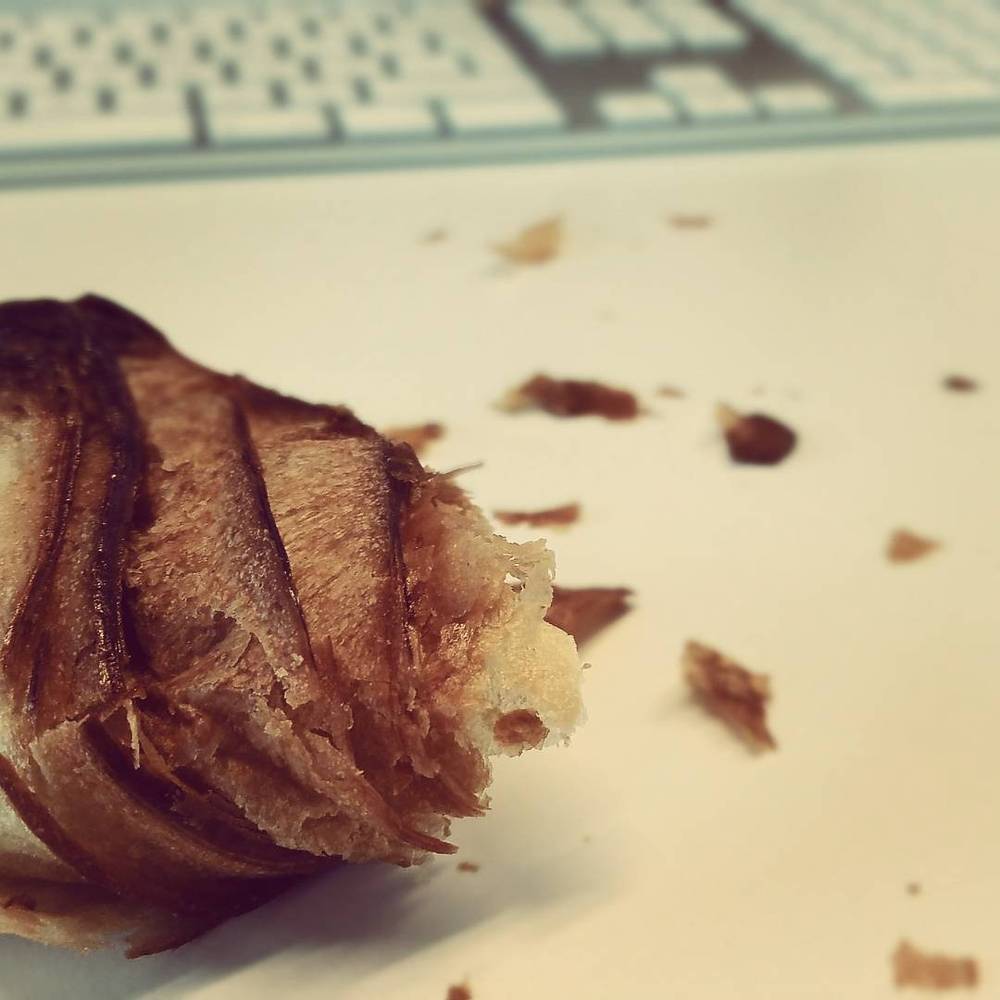 A close-up of a partly eaten croissant with crumbs scattered on a table.