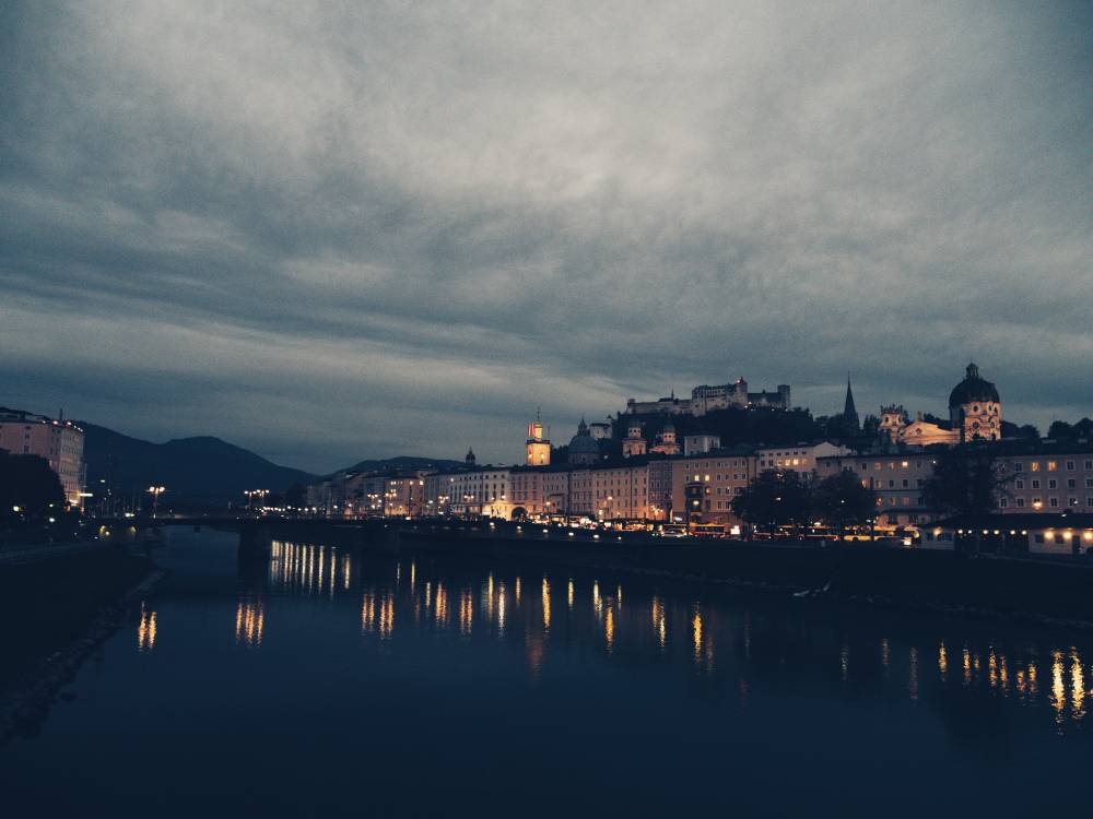 Evening in an old city. One can see a river and the city with some lights on in the buildings