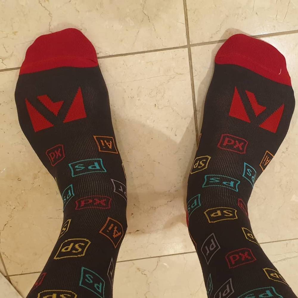 A pair of feet wearing dark socks printed with Adobe app icons like Photoshop and Illustrator.