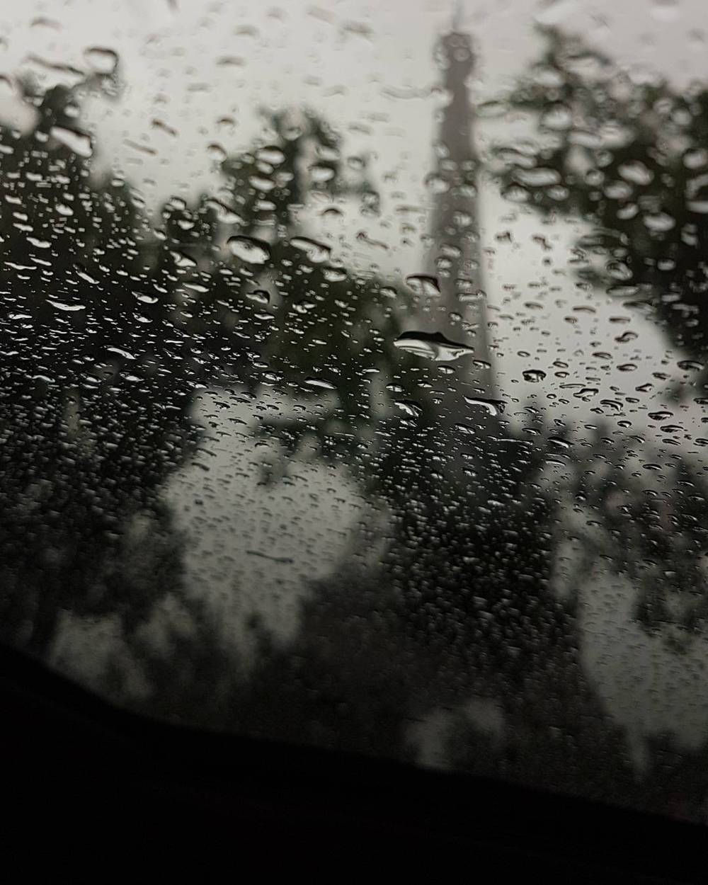 Silhouette of a tower seen through a rain-covered car window at night.