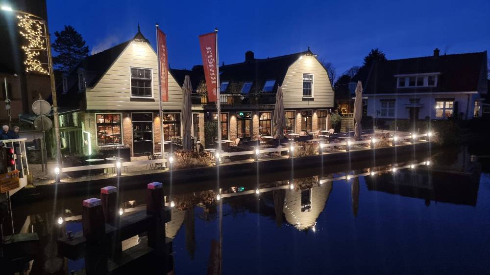 A canal-side inn lit up at night, its lights reflected in the still water.