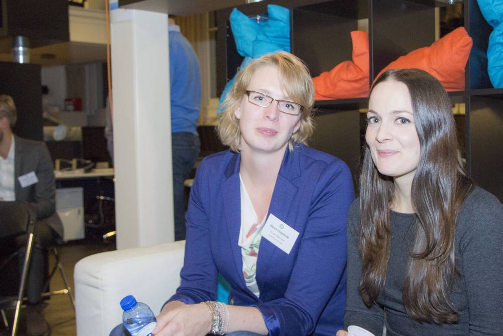 Two women chat over drinks at an indoor networking event with colourful bean bags in the background.