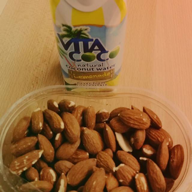 A bottle of Vita Coco coconut water lemonade next to a container of almonds.