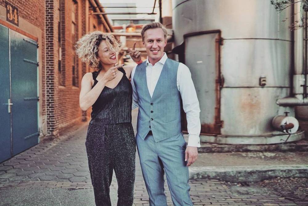 A man and woman posing together in an industrial courtyard setting.