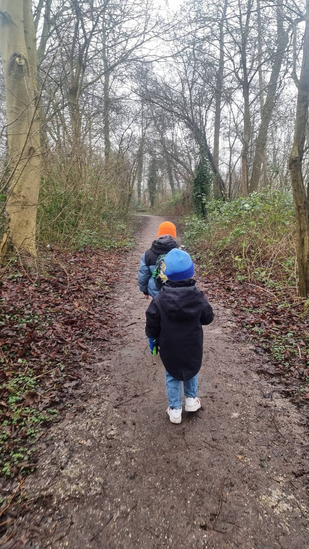 Two children walk along a muddy forest path.