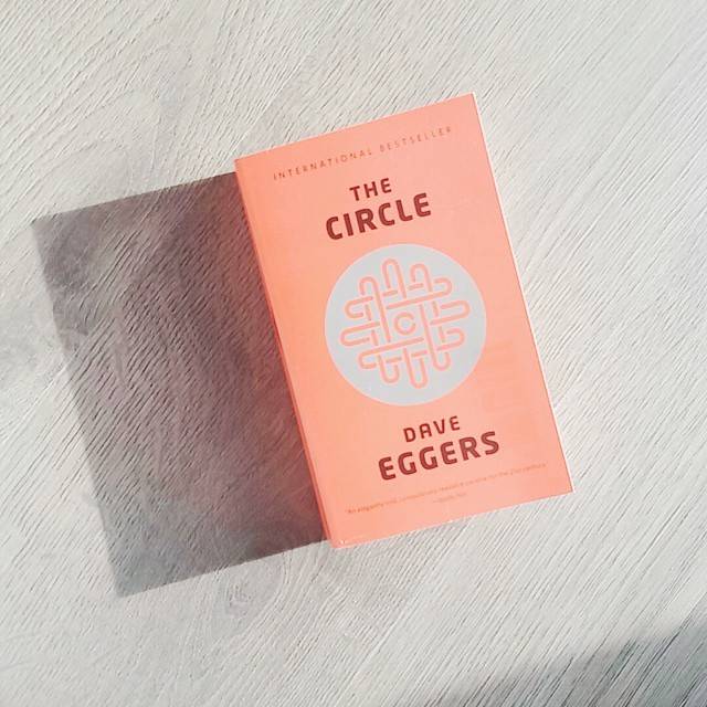 The book 'The Circle' by Dave Eggers lying on a light wooden surface.
