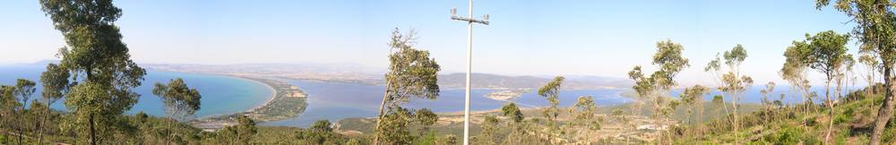 A panoramic hillside view over a coastal bay and lagoon lined with trees.
