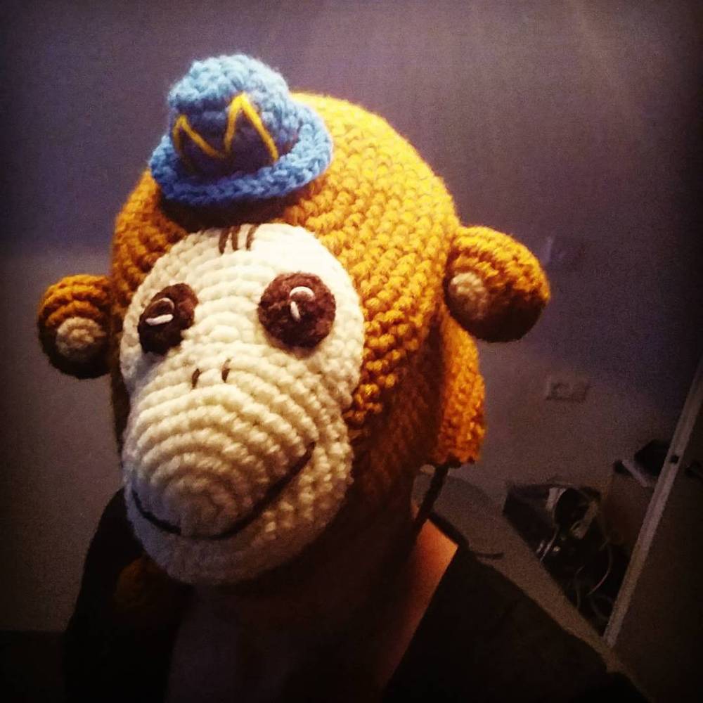 A crocheted monkey hat with a small hat detail, worn indoors.