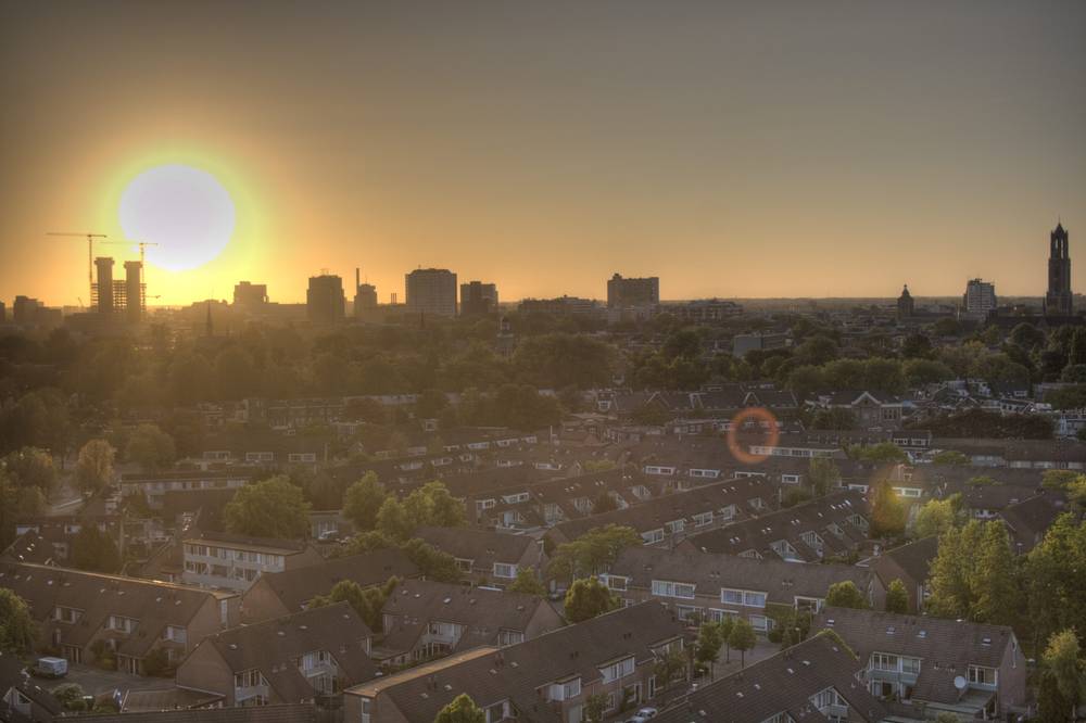 A bright sun setting over the Utrecht skyline, seen above rows of residential rooftops.