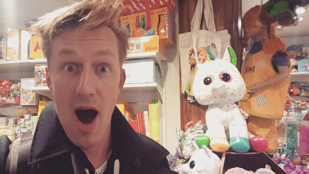 A man pulls a surprised face in a gift shop surrounded by plush toys.
