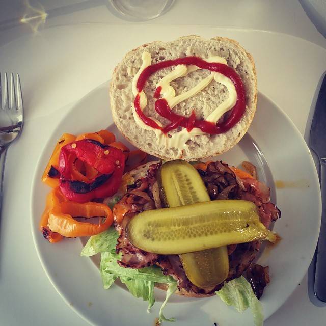 A pulled meat sandwich with roasted peppers and a pickle on a plate.