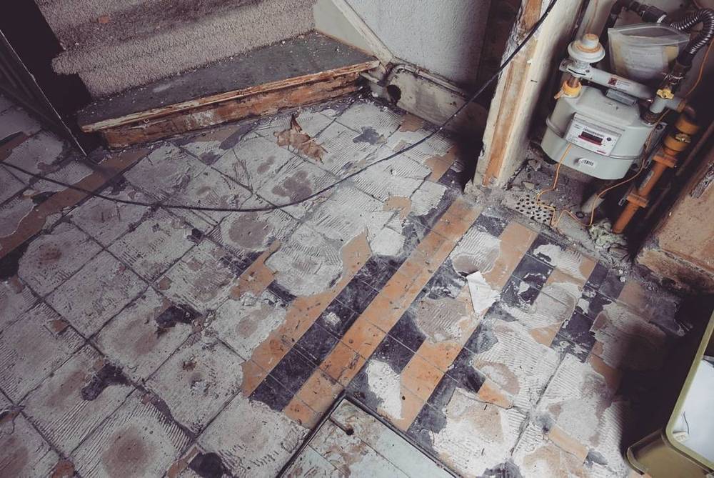 A partially stripped floor showing old tiles, exposed wiring and a gas meter.