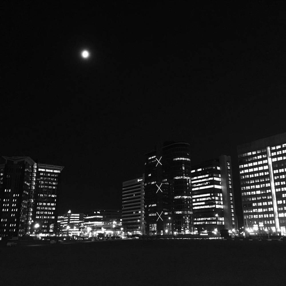 A black and white night skyline of illuminated high-rise buildings.