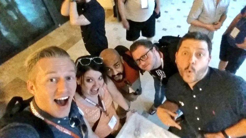 A group selfie of five people laughing together in a hotel lobby.