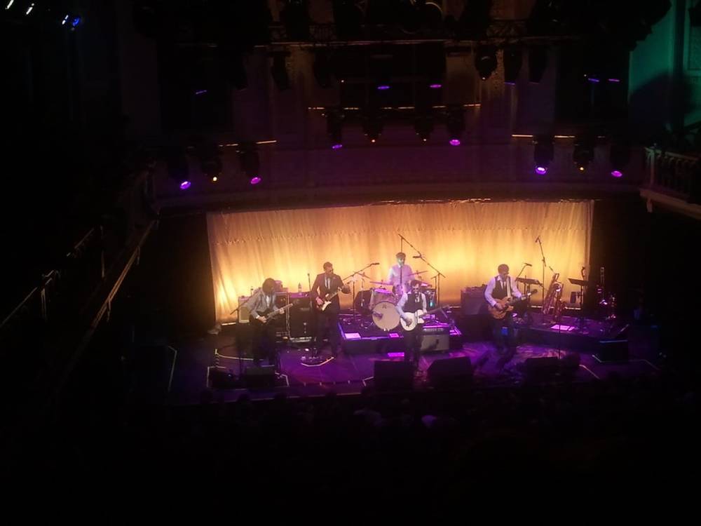 A band performs bathed in warm stage lighting at a historic concert venue.
