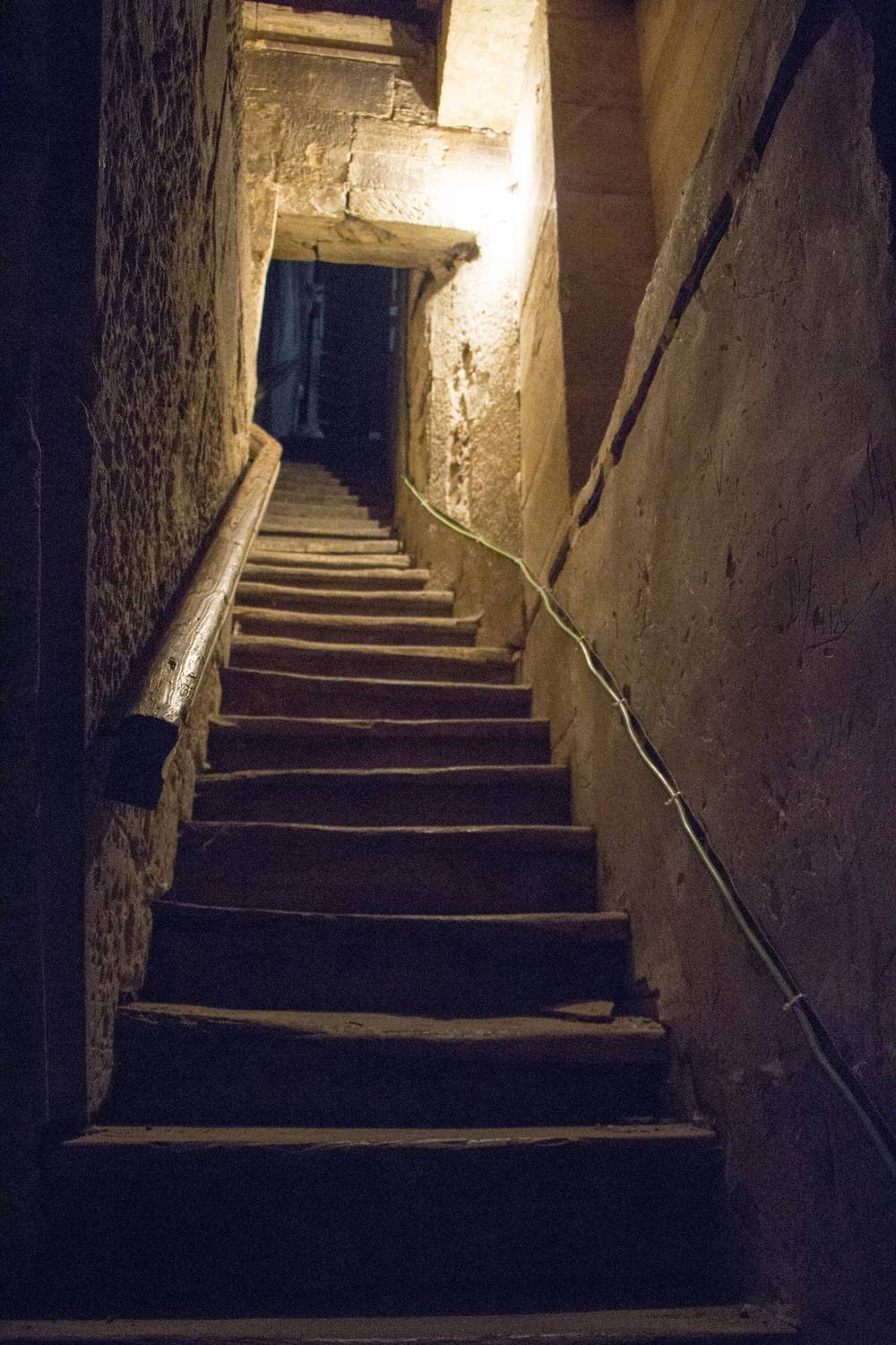 A narrow stone staircase climbs upward inside a tower, lit from above.