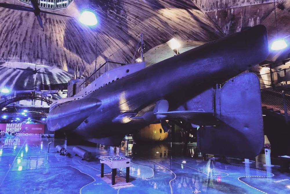 A submarine displayed inside a museum hall lit in purple, with a foosball table nearby.