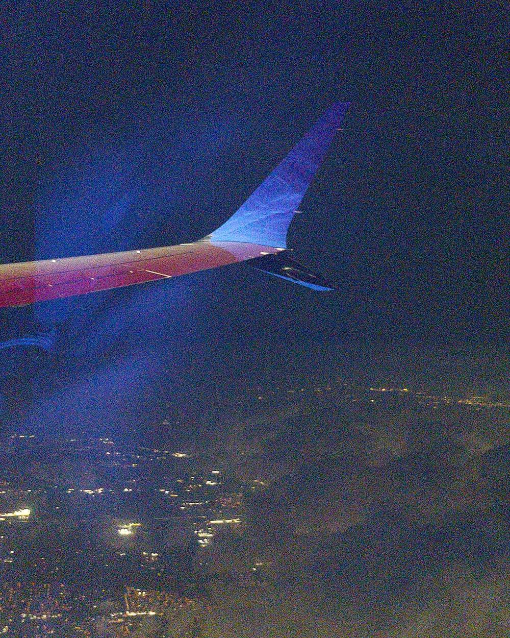 A grainy but saturated photo of a sky above clouds at night from an airplane window. The planes right wing is slightly visible.