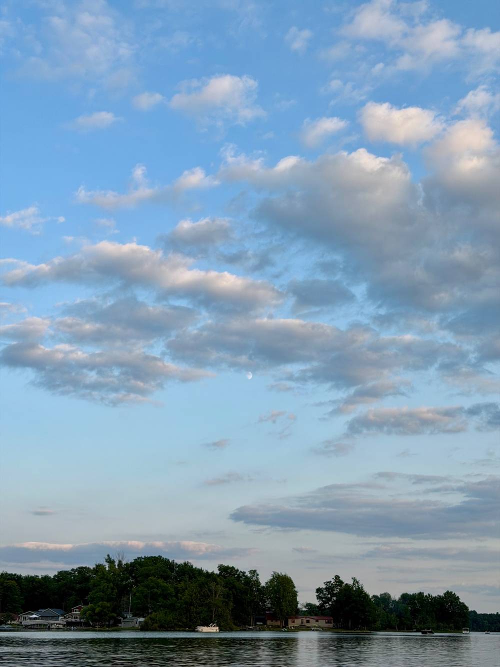 Late afternoon sky looking east over a lake in Michigan. Fluffy white and gray clouds fill up a blue sky that is just starting to develop some evening color at the horizon.