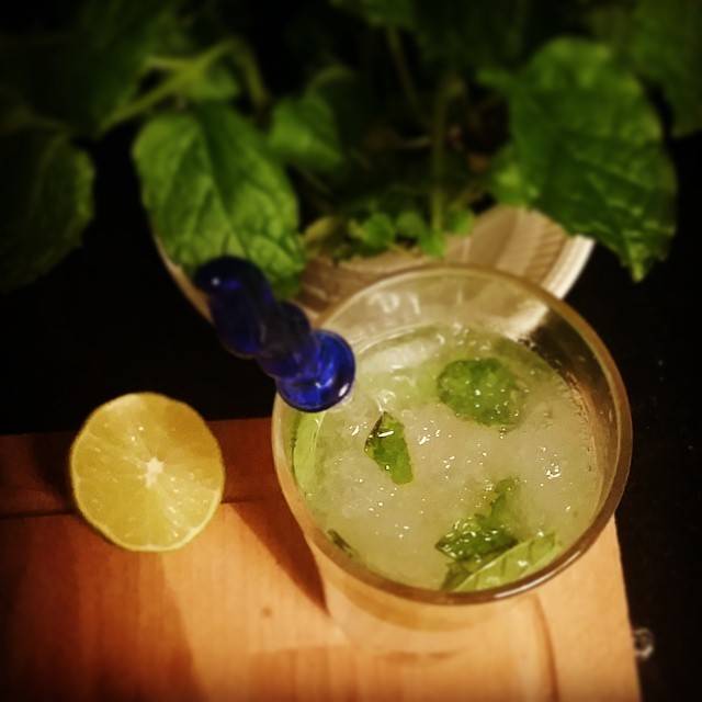 A mojito garnished with mint and a lime half on a wooden table.