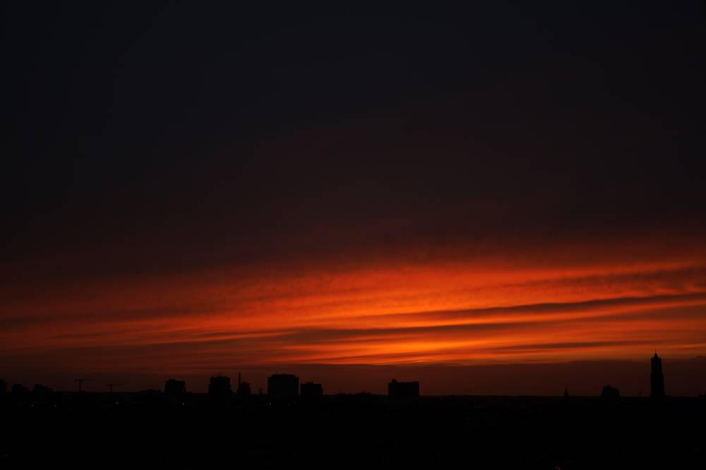 A dramatic orange-red sunset silhouetting the Utrecht skyline and church towers.