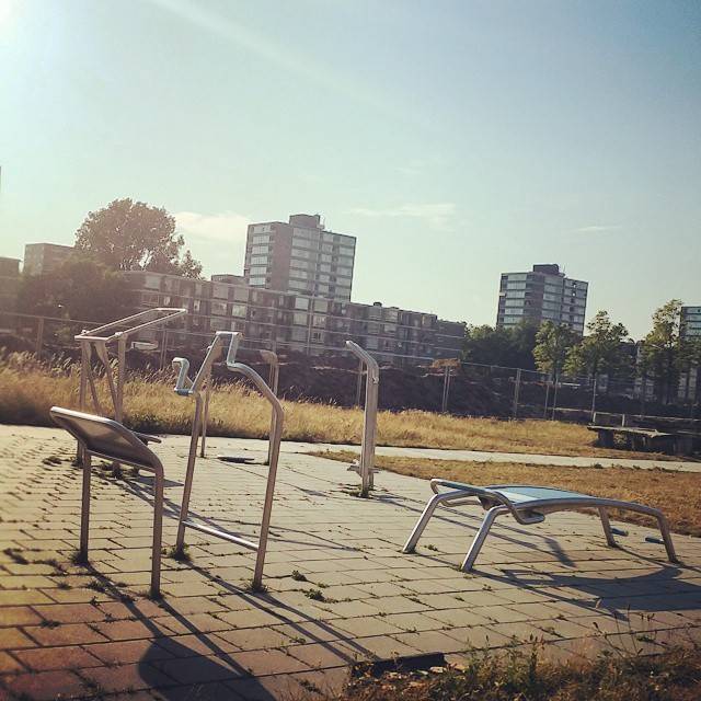 Outdoor fitness equipment on a paved area with apartment blocks in the background.