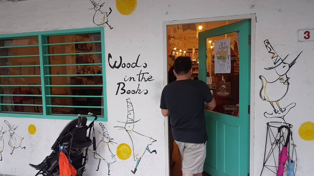 A man enters a turquoise doorway of the 'Woods in the Books' bookstore, beside a hand-drawn goose mural.