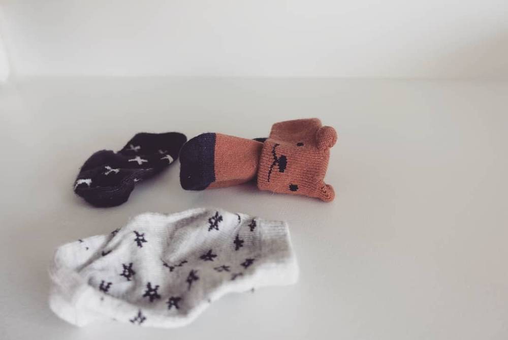 Three tiny baby socks and mittens, one shaped like a teddy bear, laid out on a table.