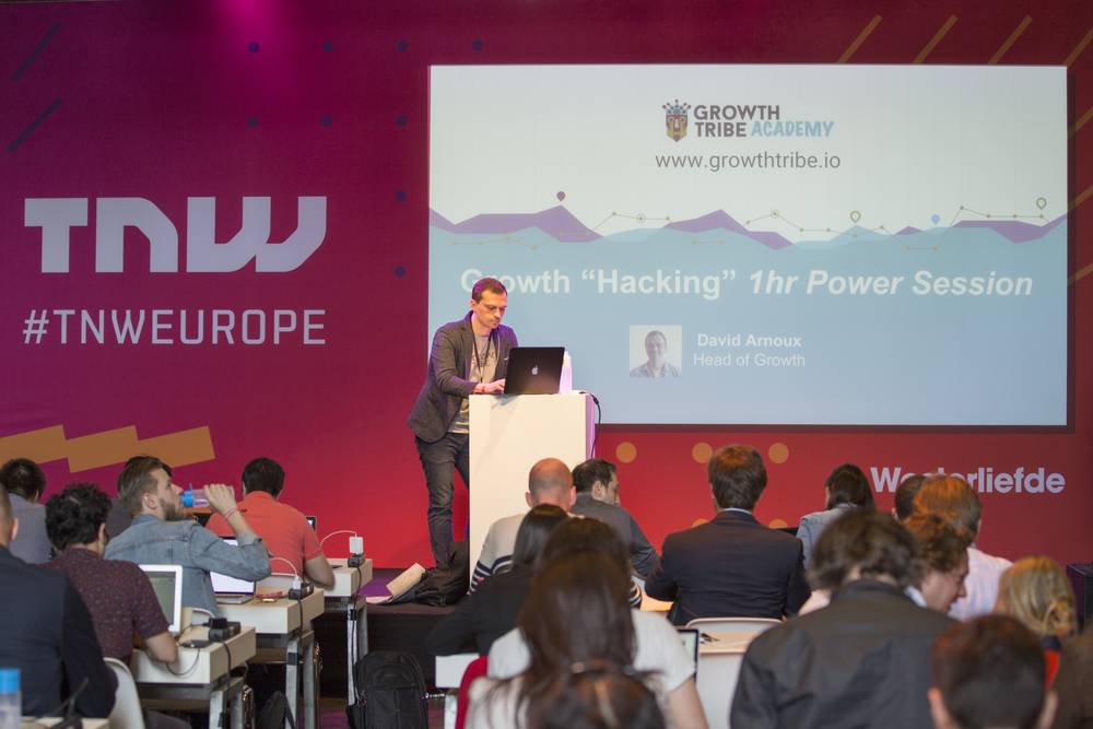 A speaker in a grey blazer gestures while presenting 'Growth Hacking 1hr Power Session' on stage.