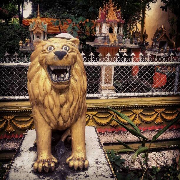 A golden lion statue in front of an ornate shrine in Vientiane.