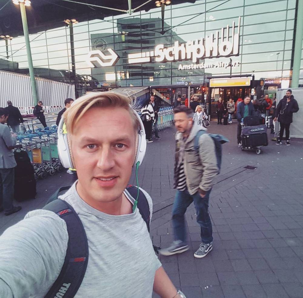 A man wearing headphones takes a selfie outside Amsterdam Schiphol Airport.