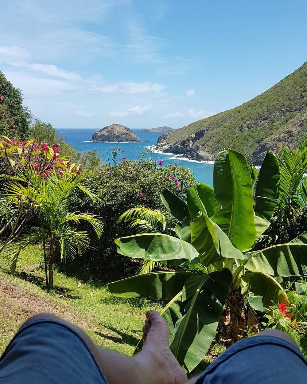 View of bare feet resting against a backdrop of tropical coastline and hills.