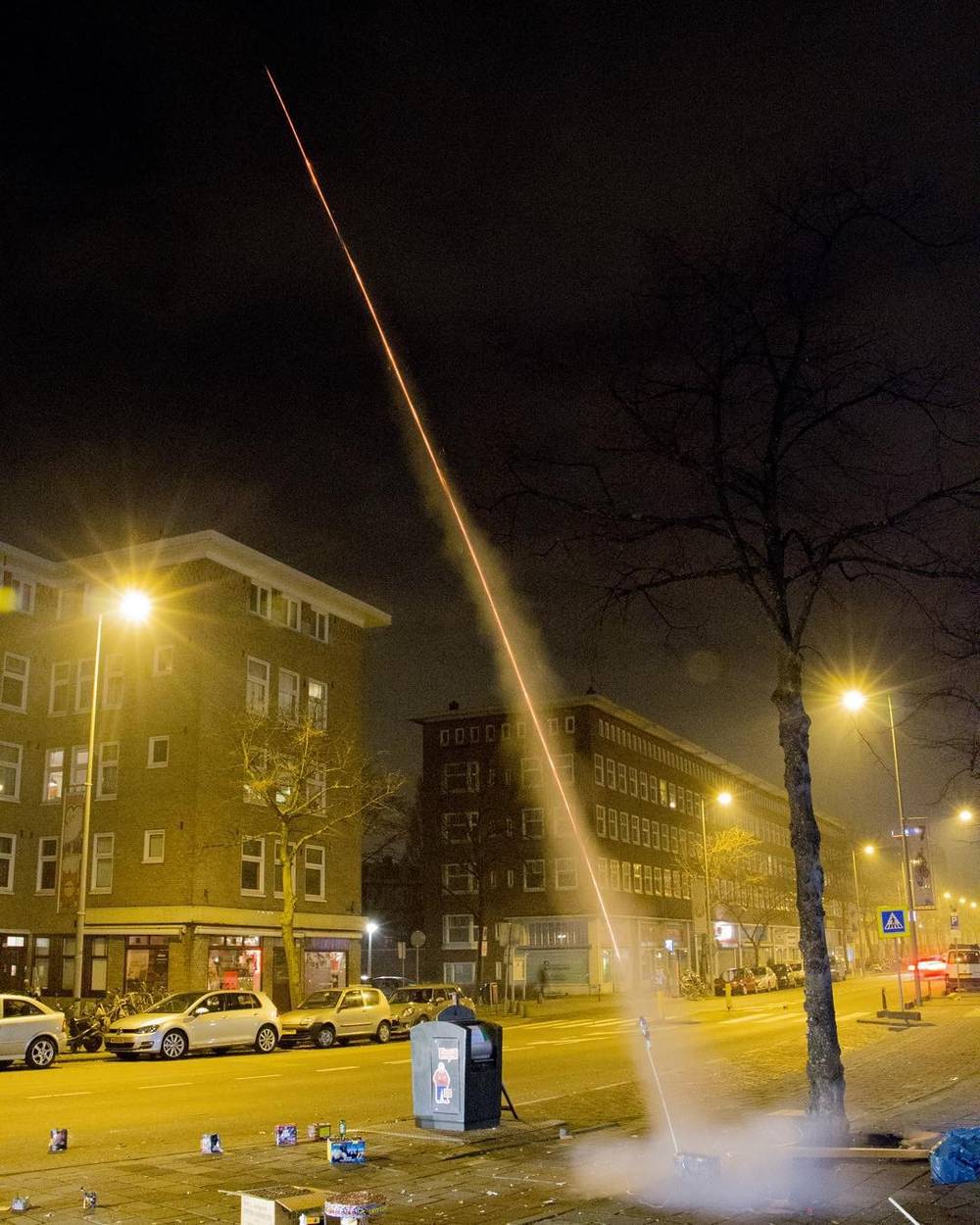 A firework rocket launching into the night sky above a street lined with buildings.