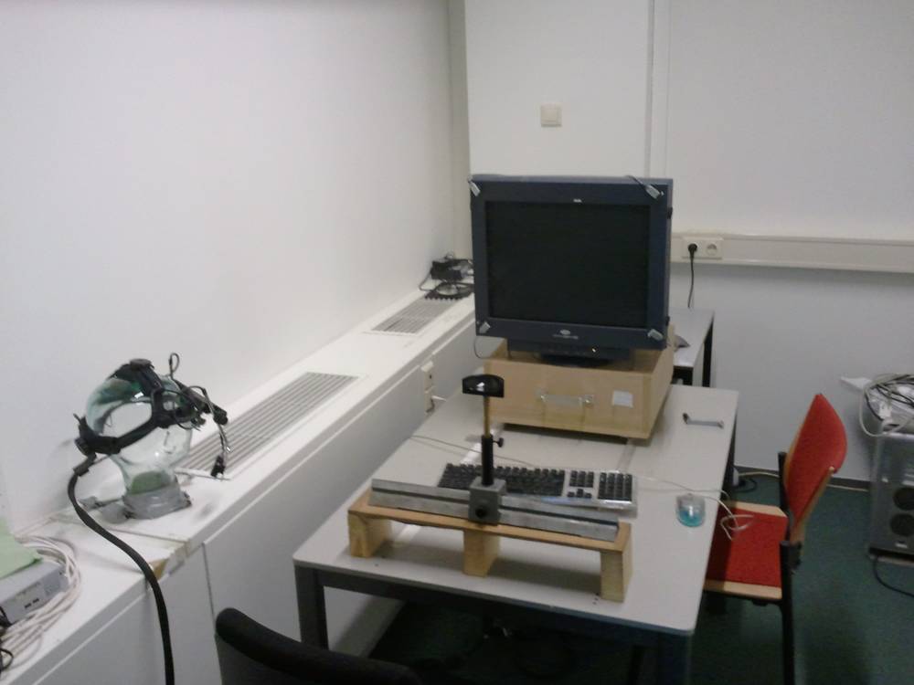 An eye-tracking headset and monitor sit set up on desks in a lab room.