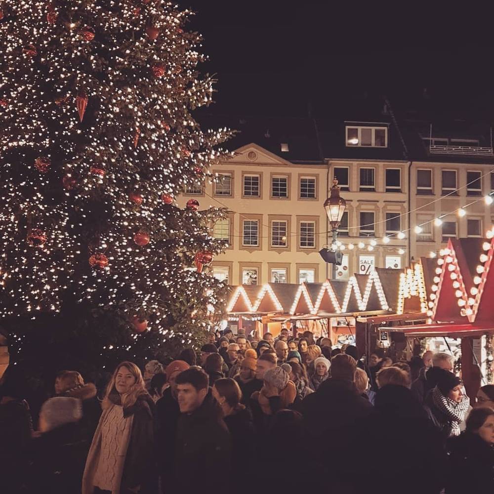 A Christmas market at night with a large decorated tree and a crowd of visitors.