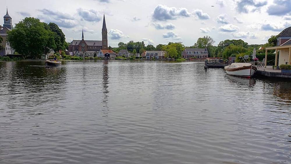 A calm river lined with houses and a church steeple, with boats moored along the bank.