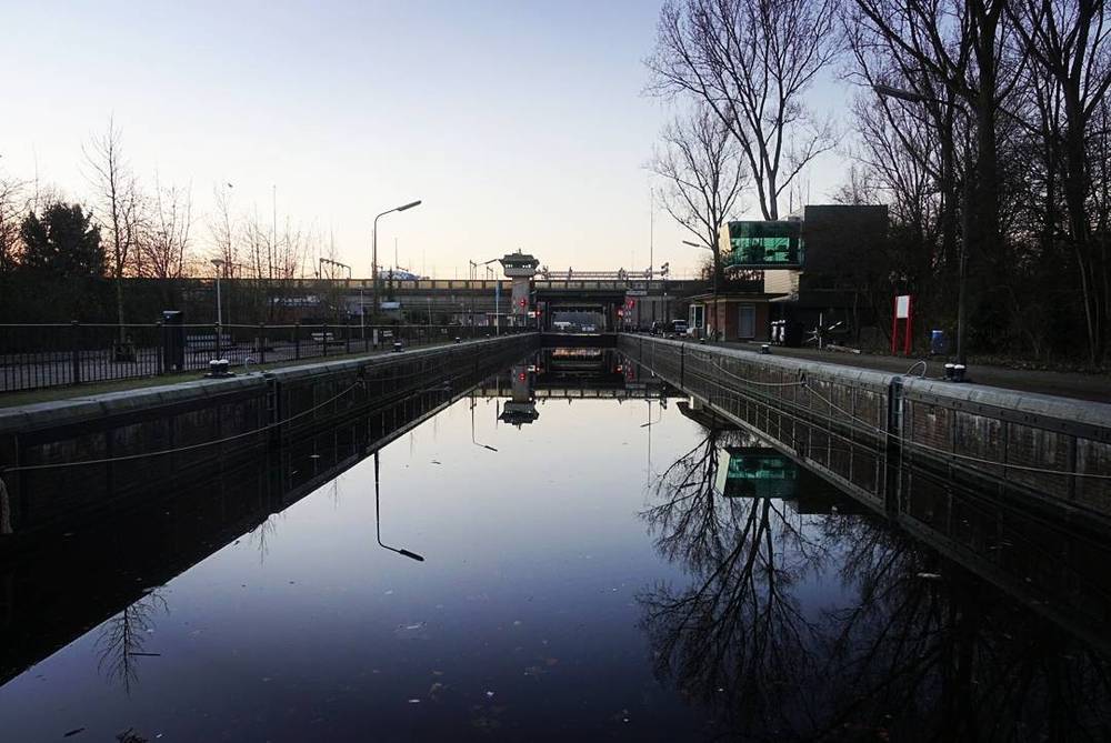 A calm canal with a bridge and buildings reflected in the still water at dawn.