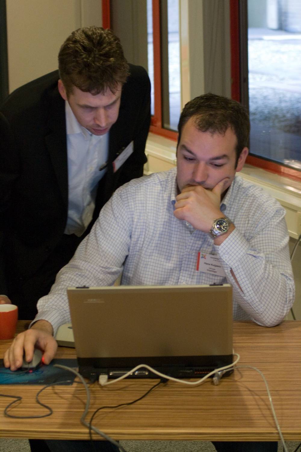 Two men in business attire look together at a laptop screen at a conference.
