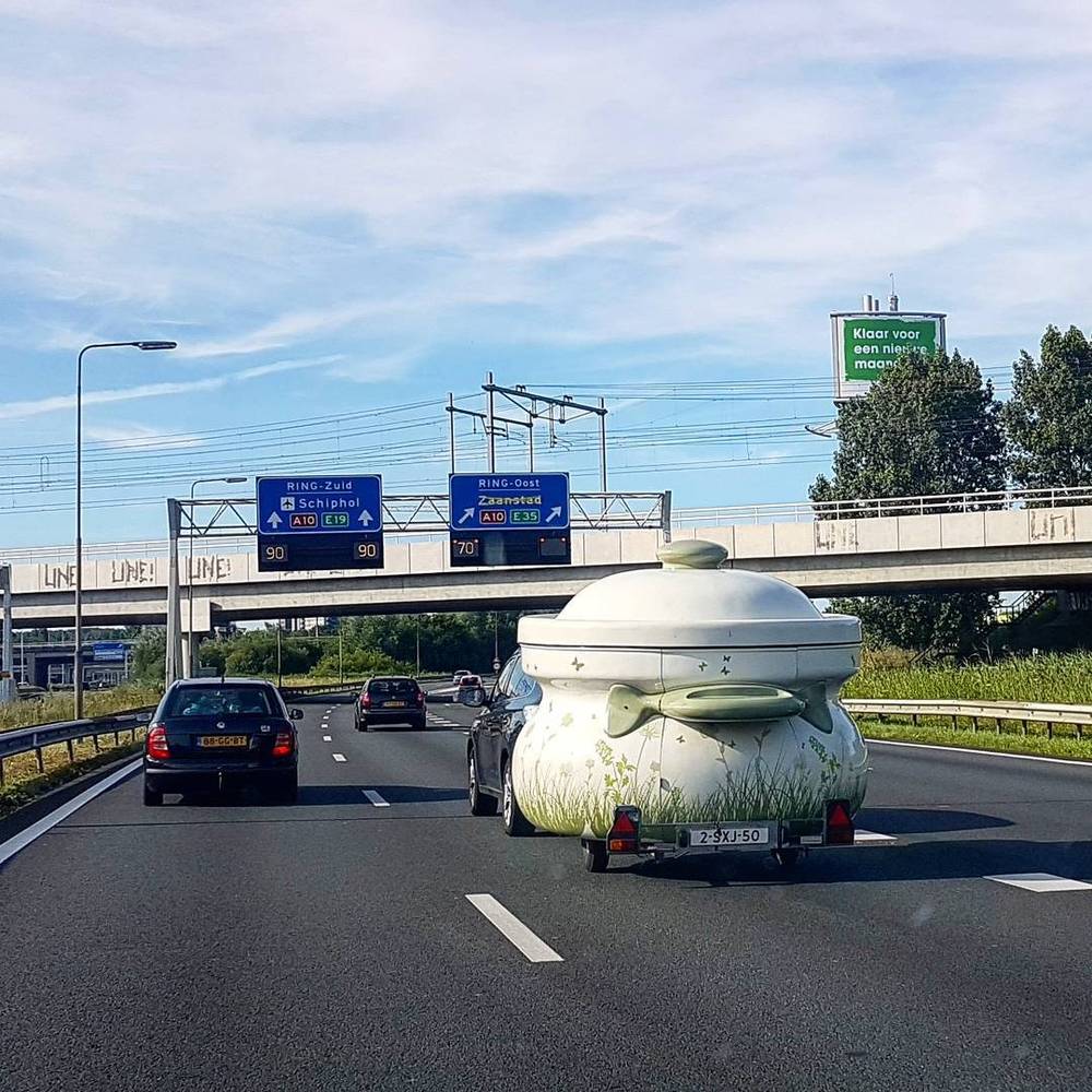 A quirky teapot-shaped caravan trailer being towed on a Dutch highway.