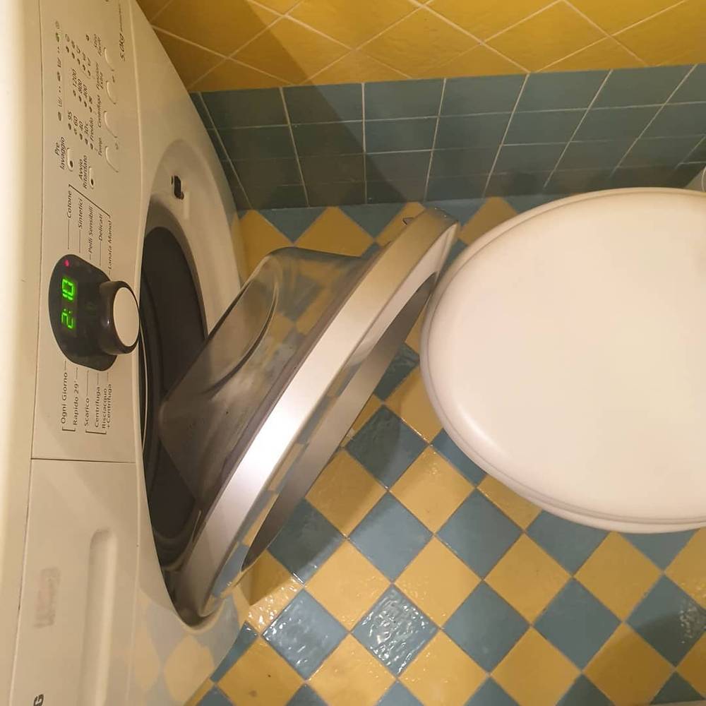 A front-loading washing machine installed right next to a toilet in a small tiled bathroom.