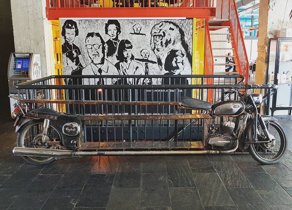 An old motorcycle with a long cargo trailer parked beside street art of faces.