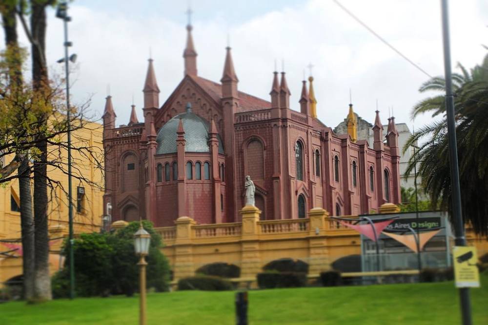 An ornate red brick Gothic-style church building behind a garden wall.