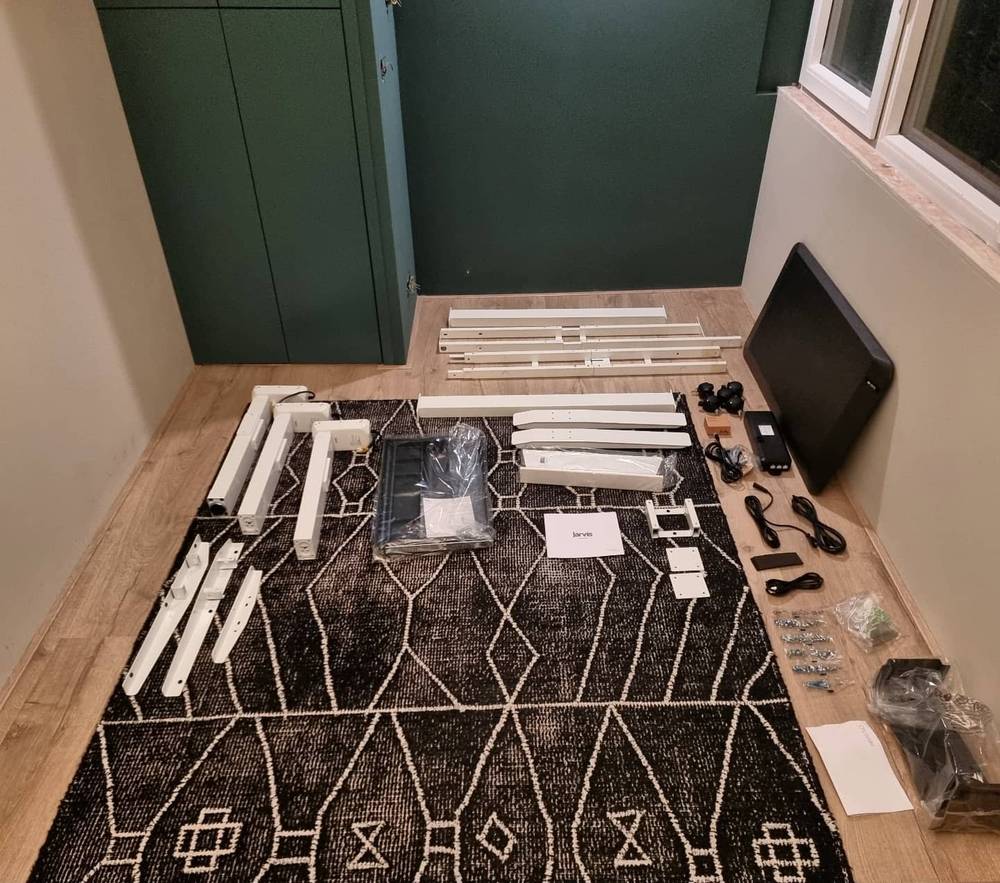 Flat-pack furniture parts, brackets, and hardware laid out on a patterned rug before assembly.
