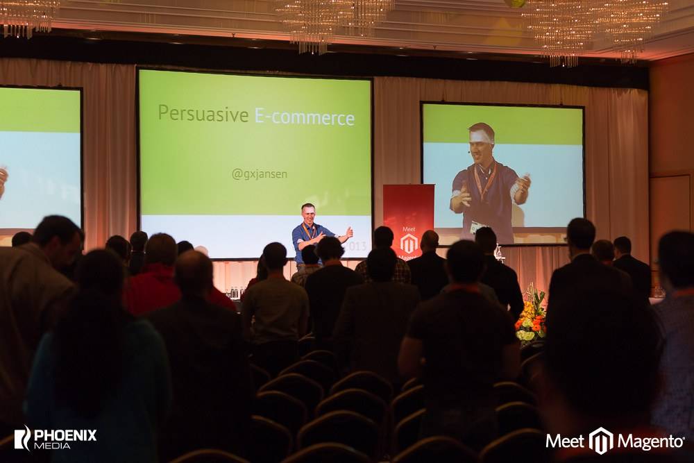 Guido presents 'Persuasive E-commerce' on stage to a packed audience at a Meet Magento conference, his Twitter handle @gxjansen shown on the screen.